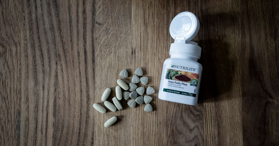 A white bottle of folic acid supplements for pregnancy dosage, with green label and capsules spilling onto a light surface.