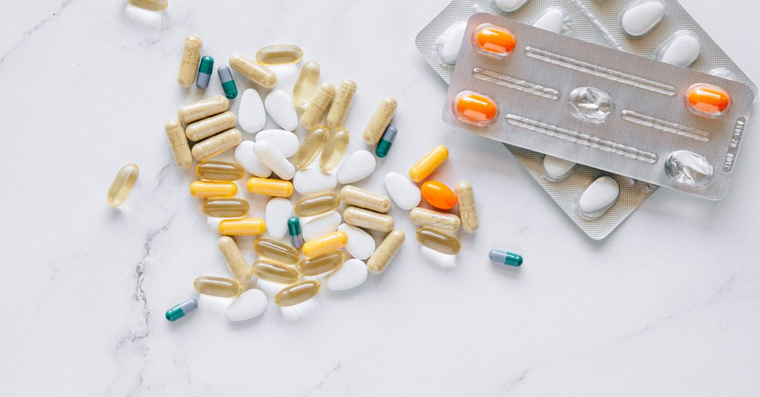 A flatlay of everyday vitamins and supplements bottles including vitamin D, omega-3, probiotics, and magnesium, on a white surface, representing an everyday vitamins & supplements buying guide.