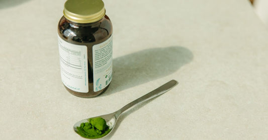 A jar of buffered vitamin C powder next to a glass of water on a kitchen bench, illustrating what is buffered vitamin C for daily routine use.